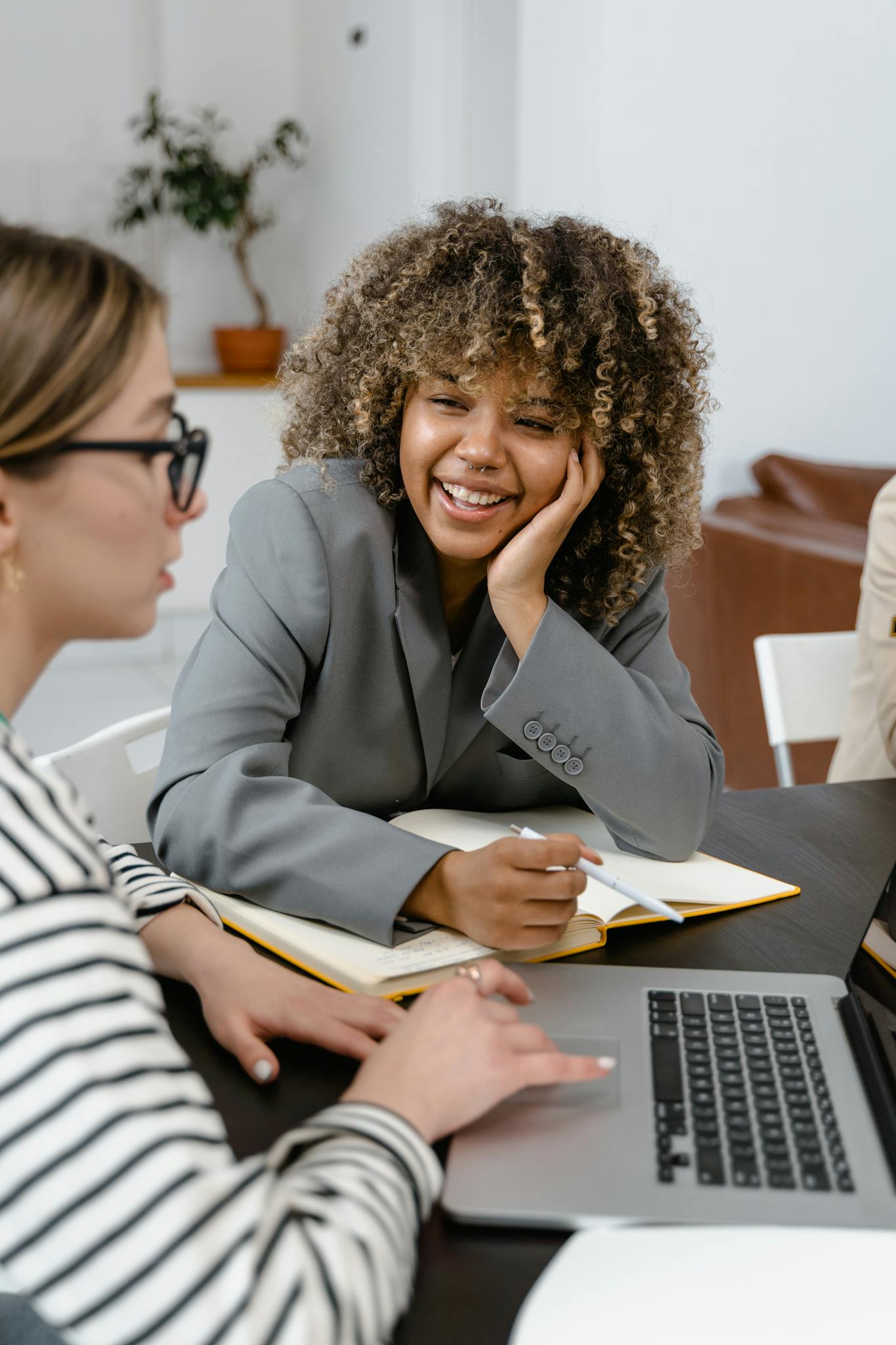 Professional women collaborating in a modern office setting with laptops and notes.
